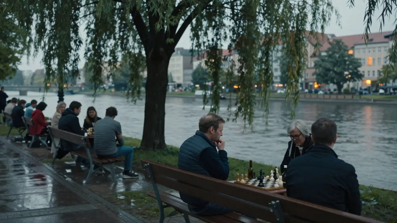 Locals sit in quiet stillness by the Spree River, playing chess under a willow tree as water ripples gently in the background.